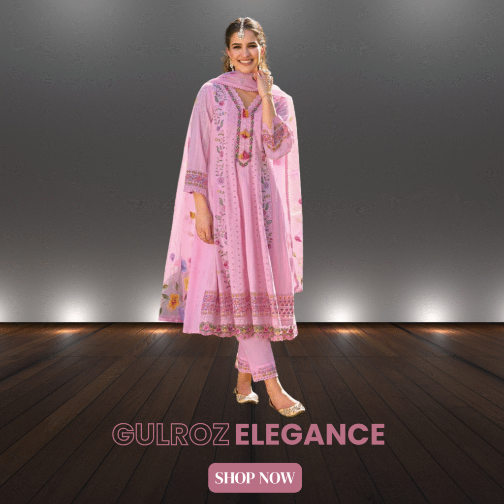 Woman wearing a traditional light pink embroidered Anarkali suit with floral patterns, matching pants, and dupatta, standing on a wooden floor with a spotlight background. Text on the image reads "GULROZ ELEGANCE" and "SHOP NOW"